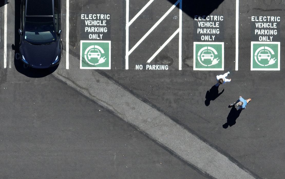 In an aerial view, pedestrians walk by an electric vehicle charging station on July 28, 2023 in Corte Madera, California. Seven major automakers announced plans earlier this year to increase the number of high-powered electric vehicle chargers in the country with 30,000 new charging stations along highways and in urban areas.